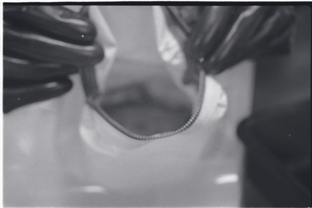 Black and white photograph of Apollo 11 Sample(s) 10010; Processing photograph displaying opening of sample bag.