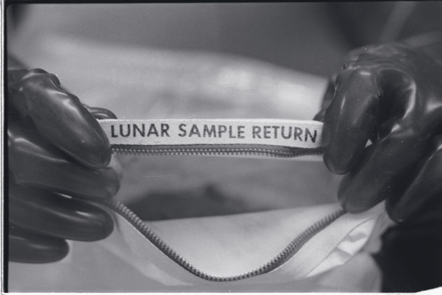 Black and white photograph of Apollo 11 Sample(s) 10010; Processing photograph displaying opening of sample bag.