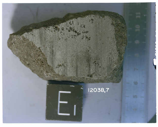 Color photograph of Apollo 12 Sample(S) 12038,7; Processing photograph displaying a slab sample with an orientation of E.