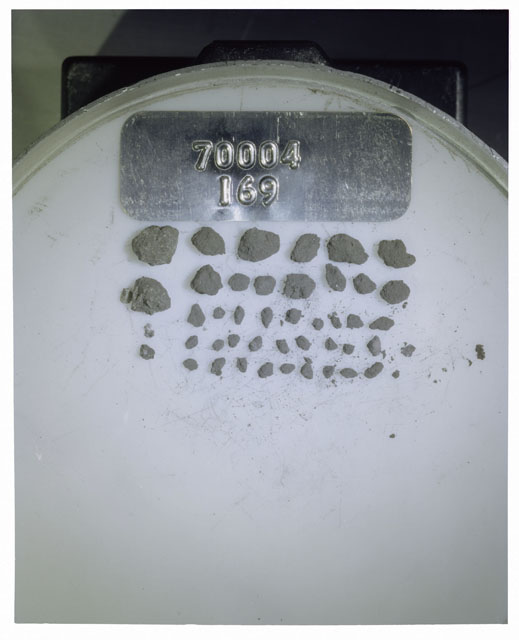 Color photograph of Apollo 17 Sample(s) 70004,169; Processing photograph displaying a group of >1 MM Core Fines found at 198.2-198.7 cm depth from surface.