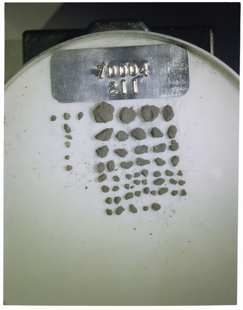 Color photograph of Apollo 17 Sample(s) 70004,211; Processing photograph displaying a group of >1 MM Core Fines found at 208.2-208.7 cm depth from surface.