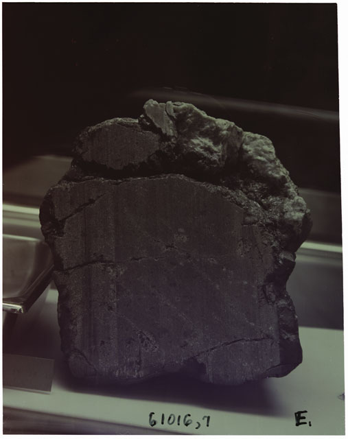 Black and white photograph of Apollo 16 Sample(s) 61016,7; Processing photograph displaying sawed surface with an orientation of E.