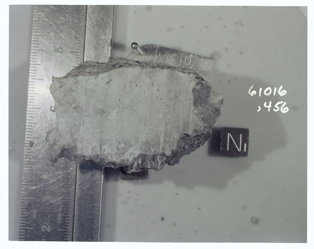 Color photograph of Apollo 16 Sample(s) 61016,456; Processing photograph displaying sawed surface with an orientation of N.